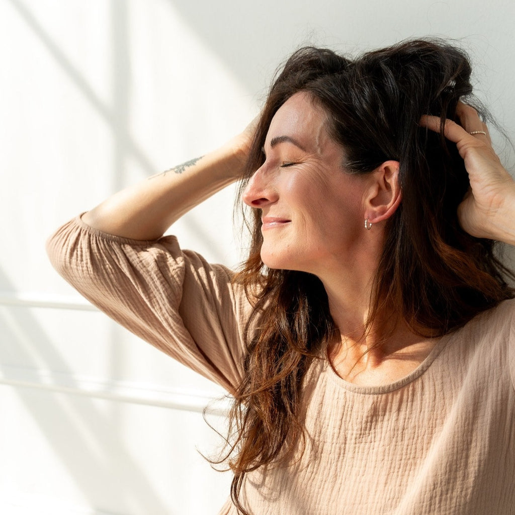 Woman sitting in the sun rays from a nearby window.  She is wearing sterling silver beaded mini hoop earrings and a sterling silver beaded ring