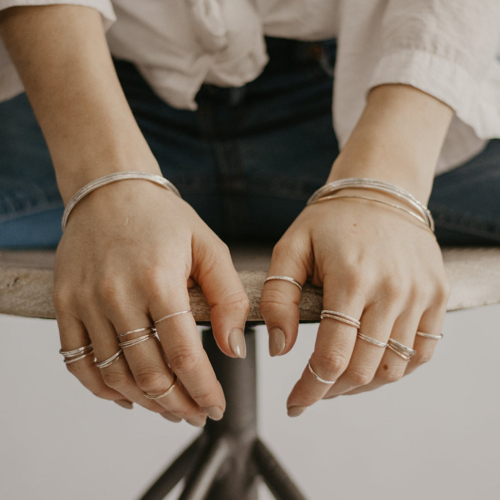 Woman wearing minimalist handmade sterling silver and 14k solid gold stacking bangles and rings