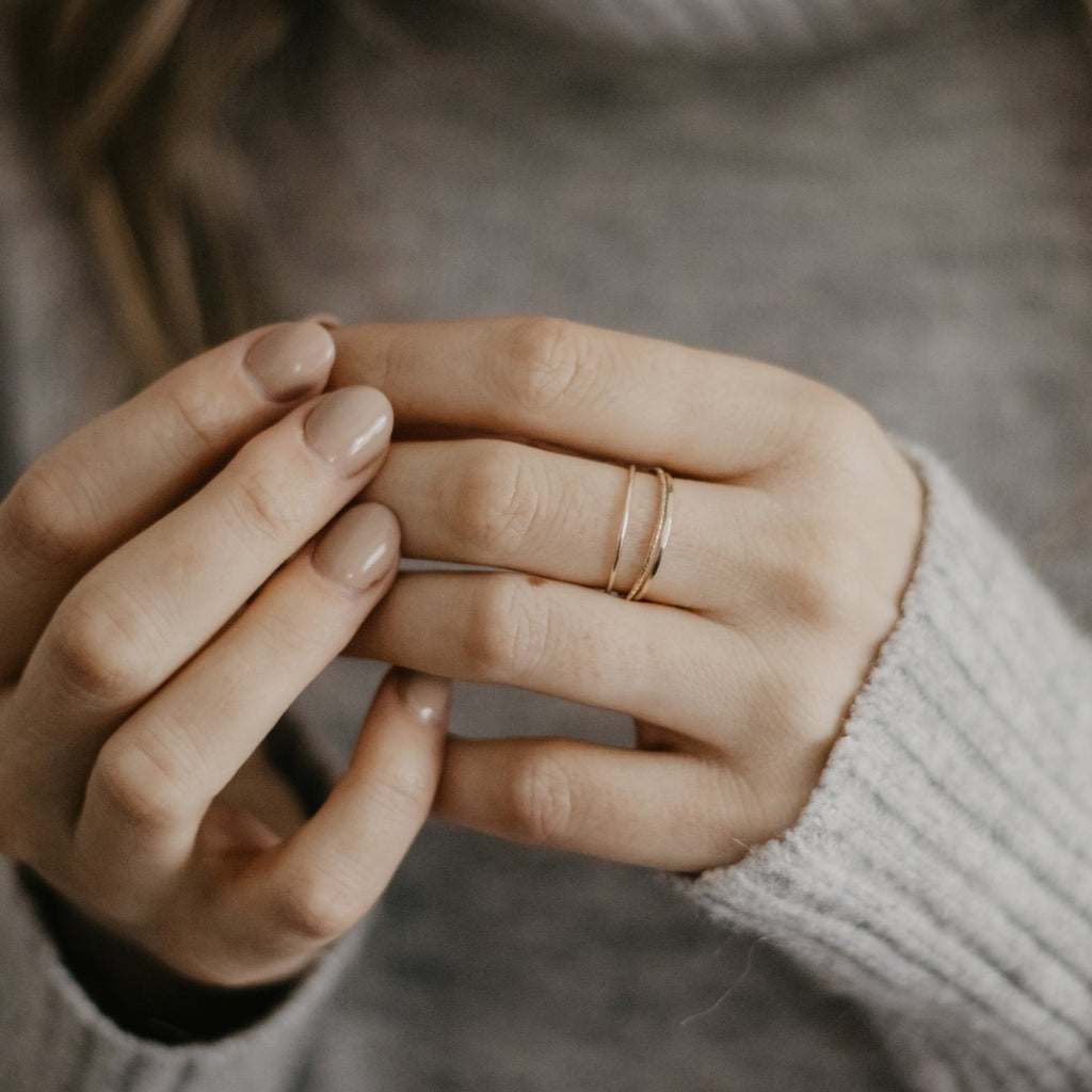 Hands wearing minimalist handmade 14k solid gold stacking rings with in a smooth birch and faceted texture