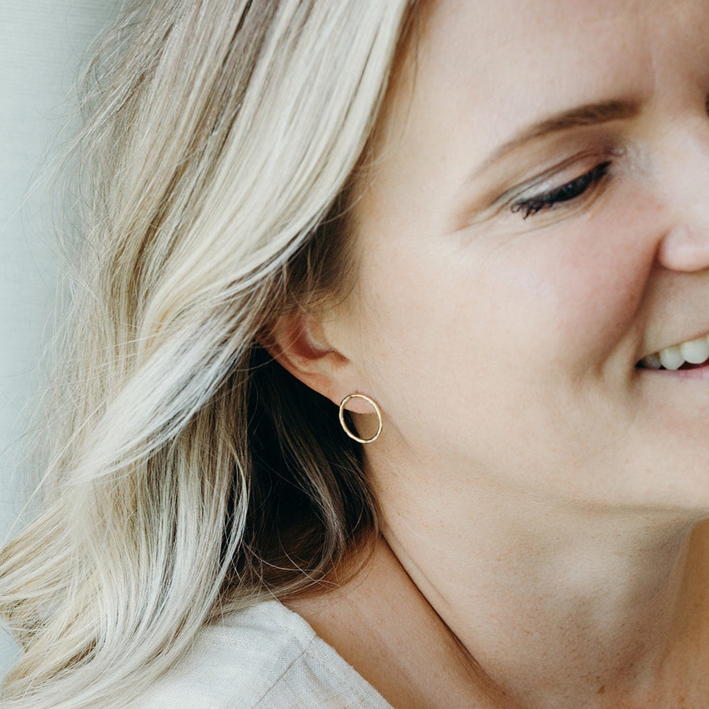 Woman wearing solid 14k gold 'Water Circle' stud earrings with a hammered finish