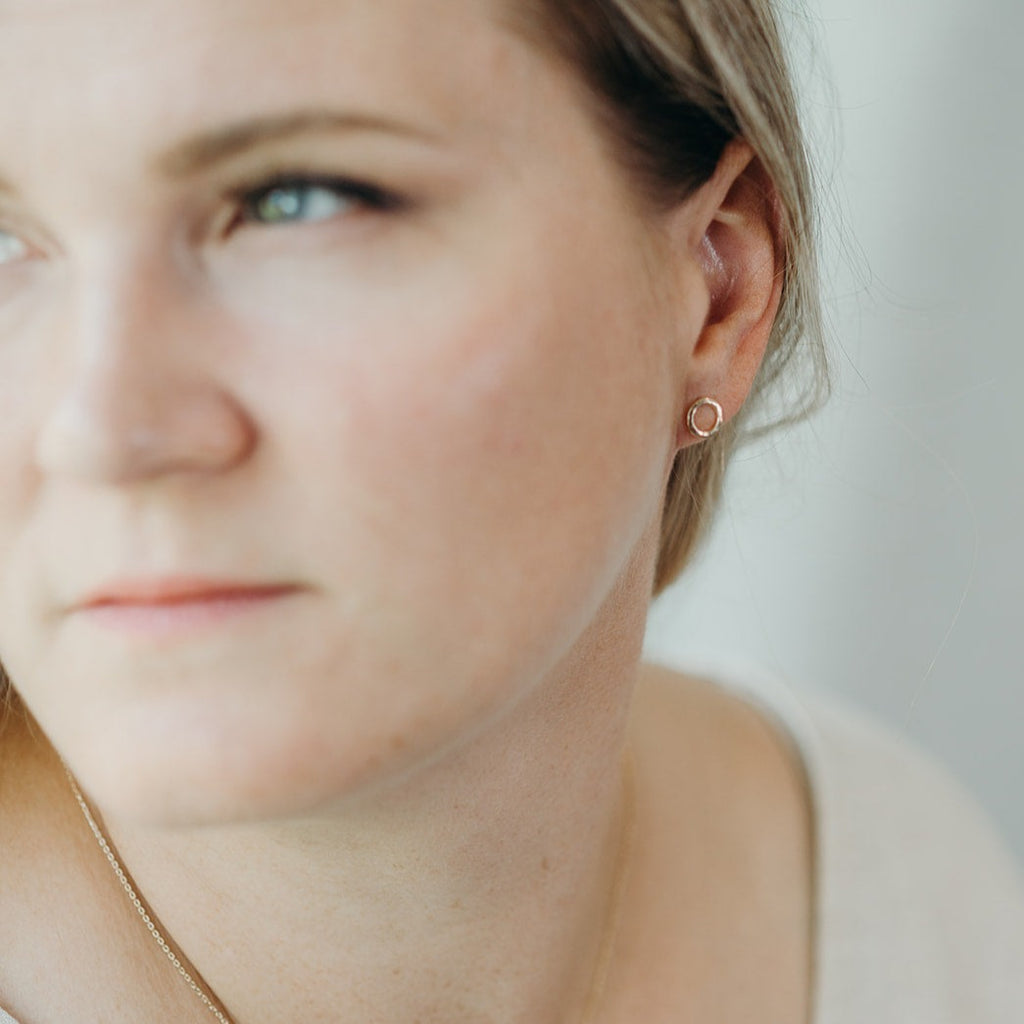 Woman wearing minimalist handmade 14k solid gold 'Water Circle' stud earring in a hammered finish