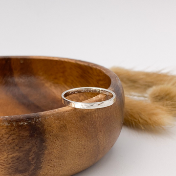 A Sterling Silver 2.5mm band with a hammered texture resting on a wooden bowl. On the inside of the ring it says 'You Got This'